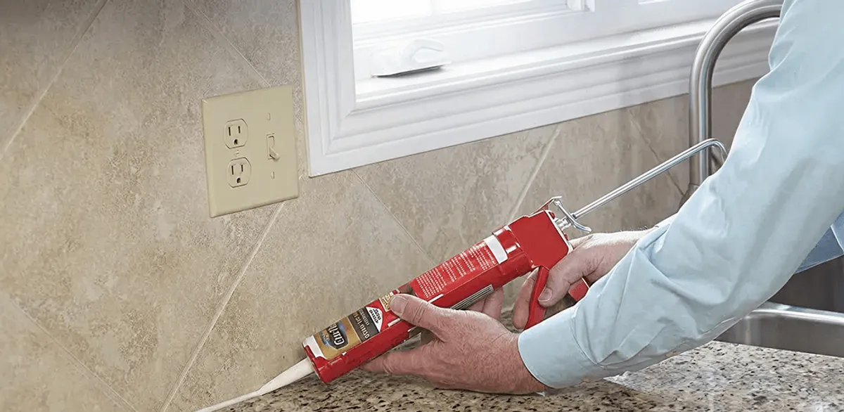 Handyman applying caulk along a kitchen backsplash and countertop seam in Oklahoma City, OK